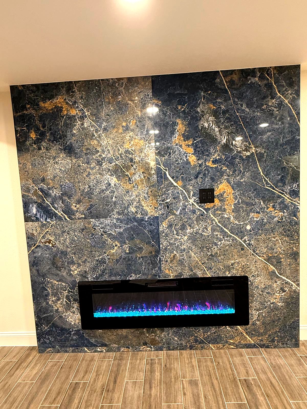The finished blue and gold slab feature wall with a linear electric fireplace set flush into the stone, over wood-look plank tile
