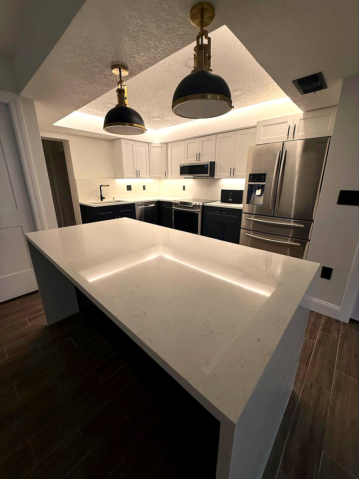 Quartz waterfall island with a navy base under two black and brass dome pendants