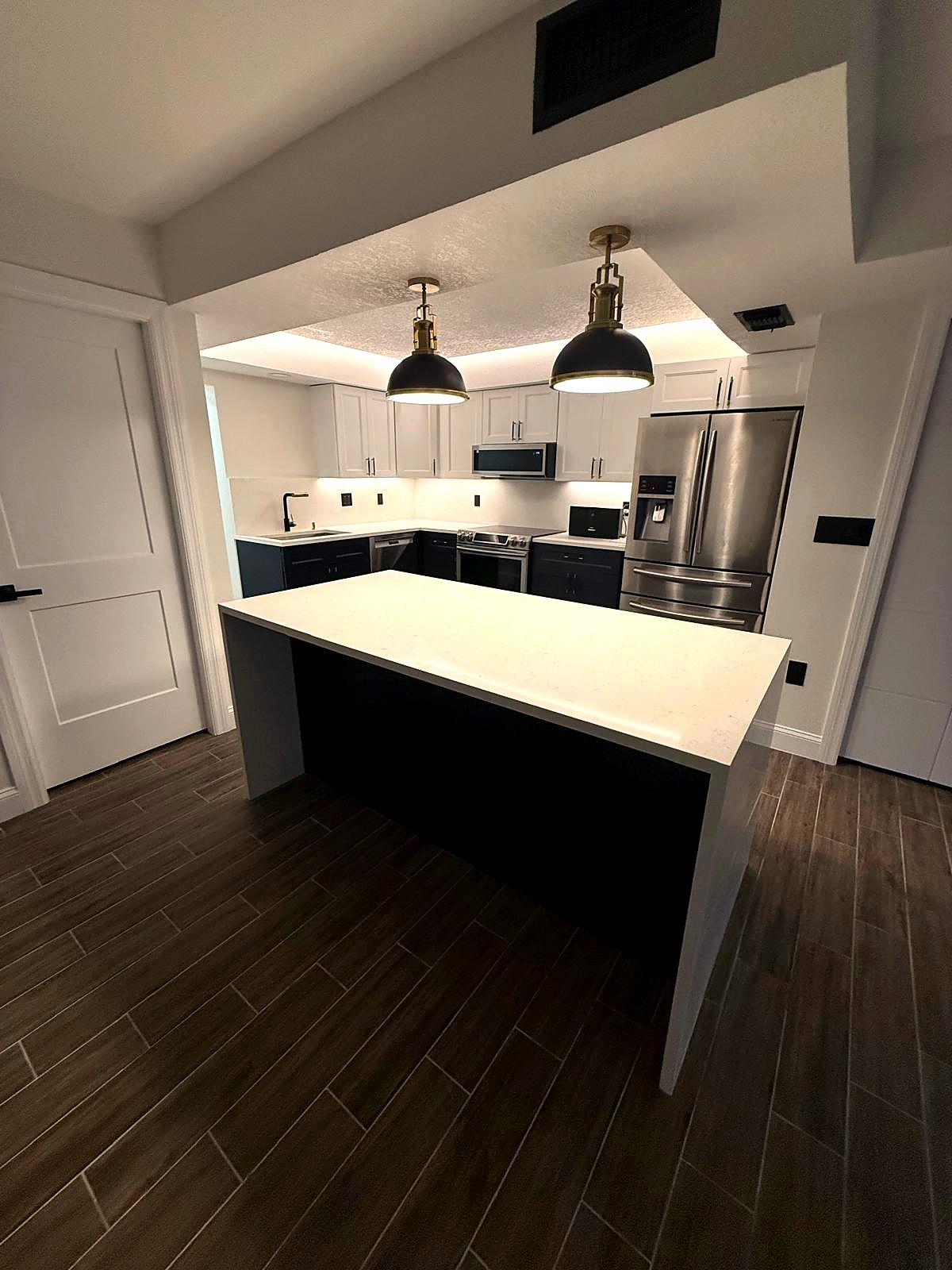 The finished kitchen: navy lower cabinets, white uppers, stainless appliances and a quartz waterfall island