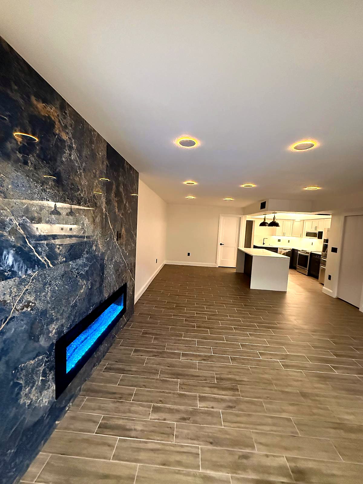 The living room from the fireplace end, recessed halo lights running toward the kitchen