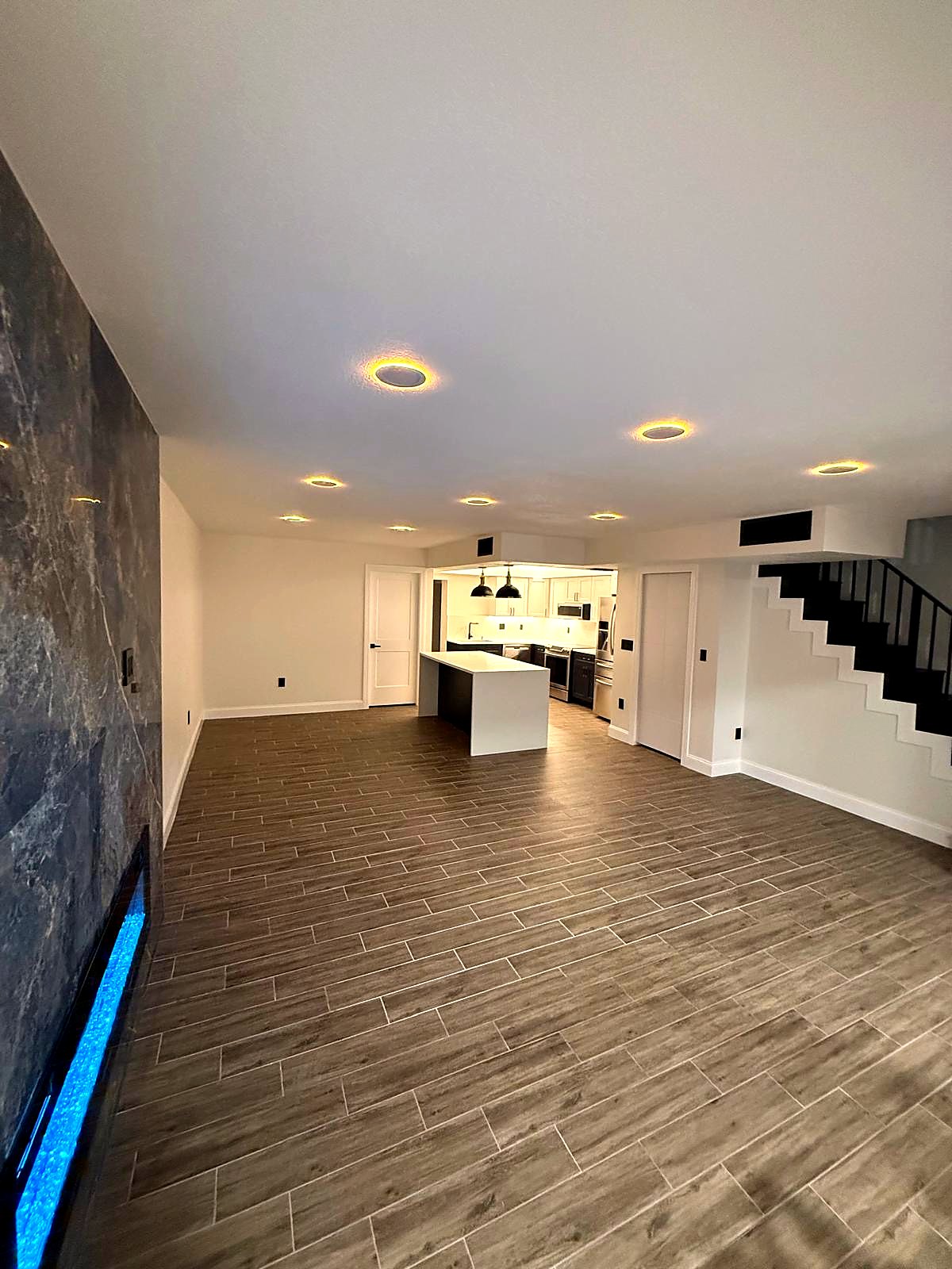Open plan from the fireplace wall to the kitchen island and a black-railed staircase
