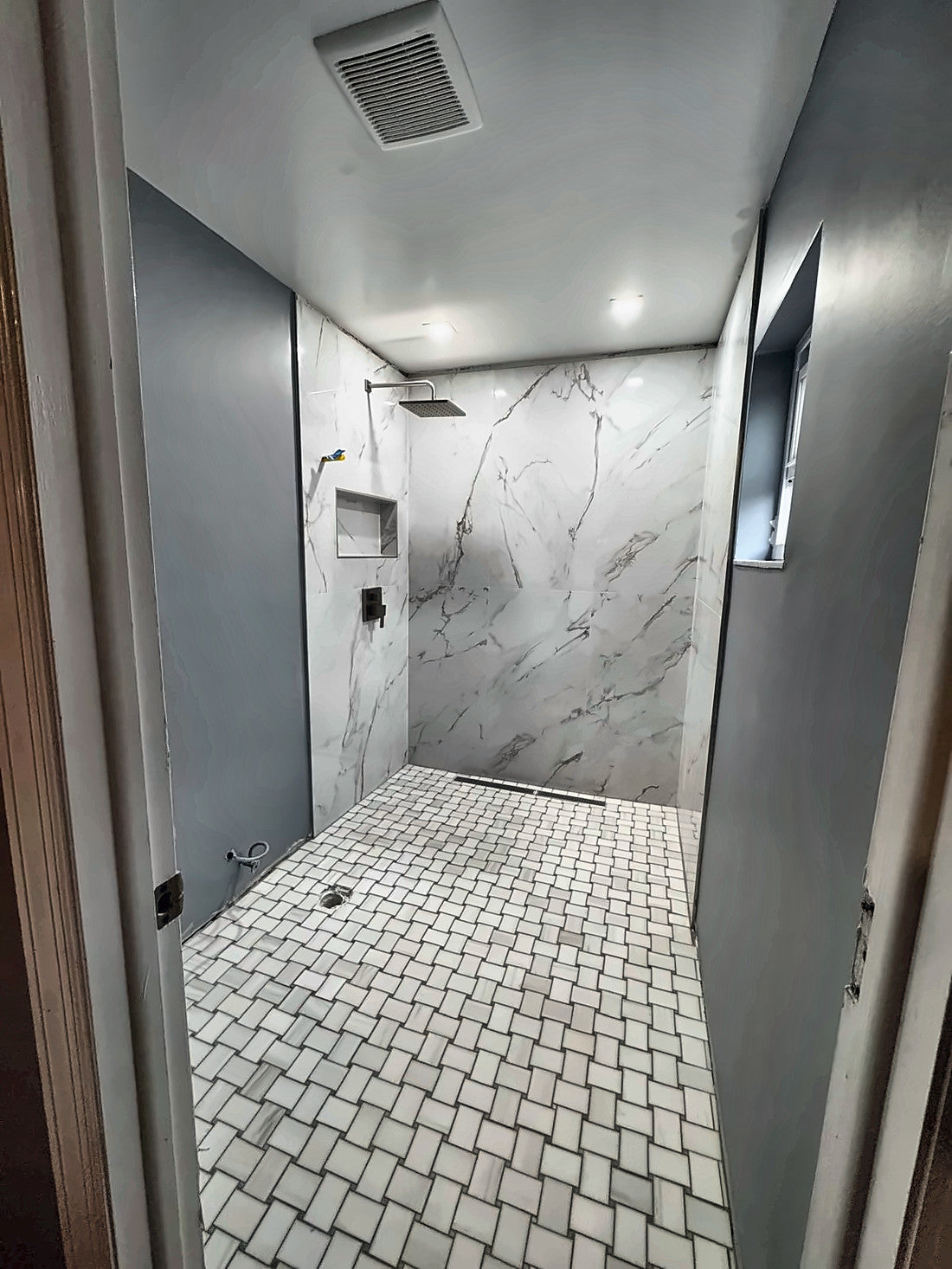 The finished walk-in shower with marble-look slab walls, basketweave mosaic floor, rain head and linear drain