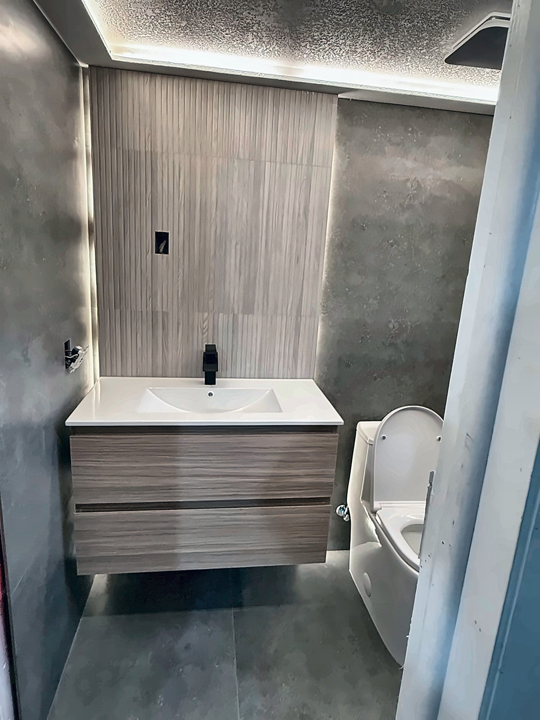 Powder room with a fluted wood-look feature wall, concealed cove light running the ceiling perimeter, floating timber vanity and a matte black tap