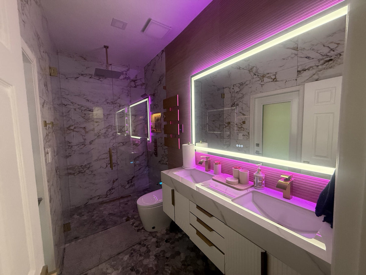 Bathroom in white marble-look tile with gold veining, a frameless glass shower with brass hardware, hexagon mosaic floor and a fluted double floating vanity under a lit mirror