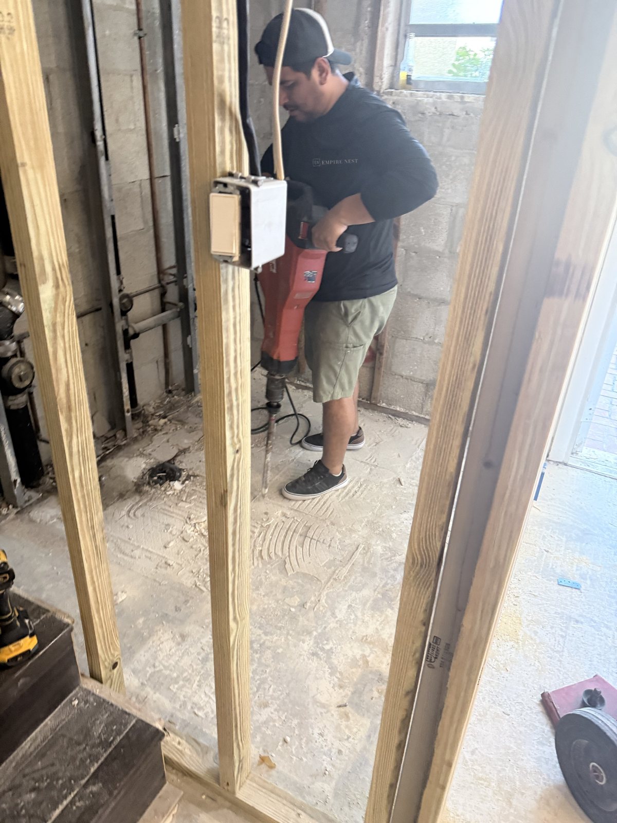 A worker in an Empire Nest shirt running a demolition hammer on the old floor inside a framed wall