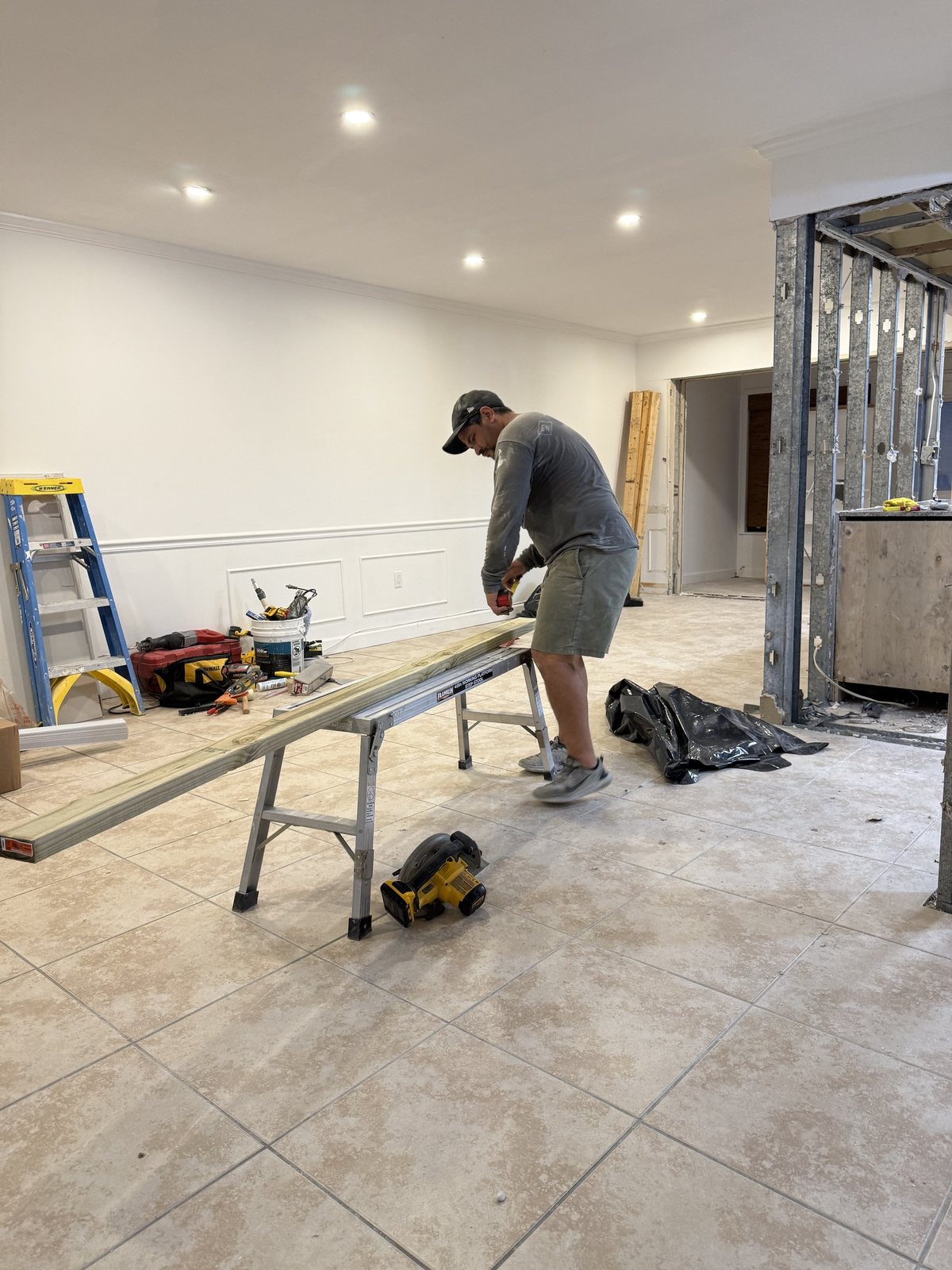 A worker in an Empire Nest shirt cutting a long board on a saw stand in a white room