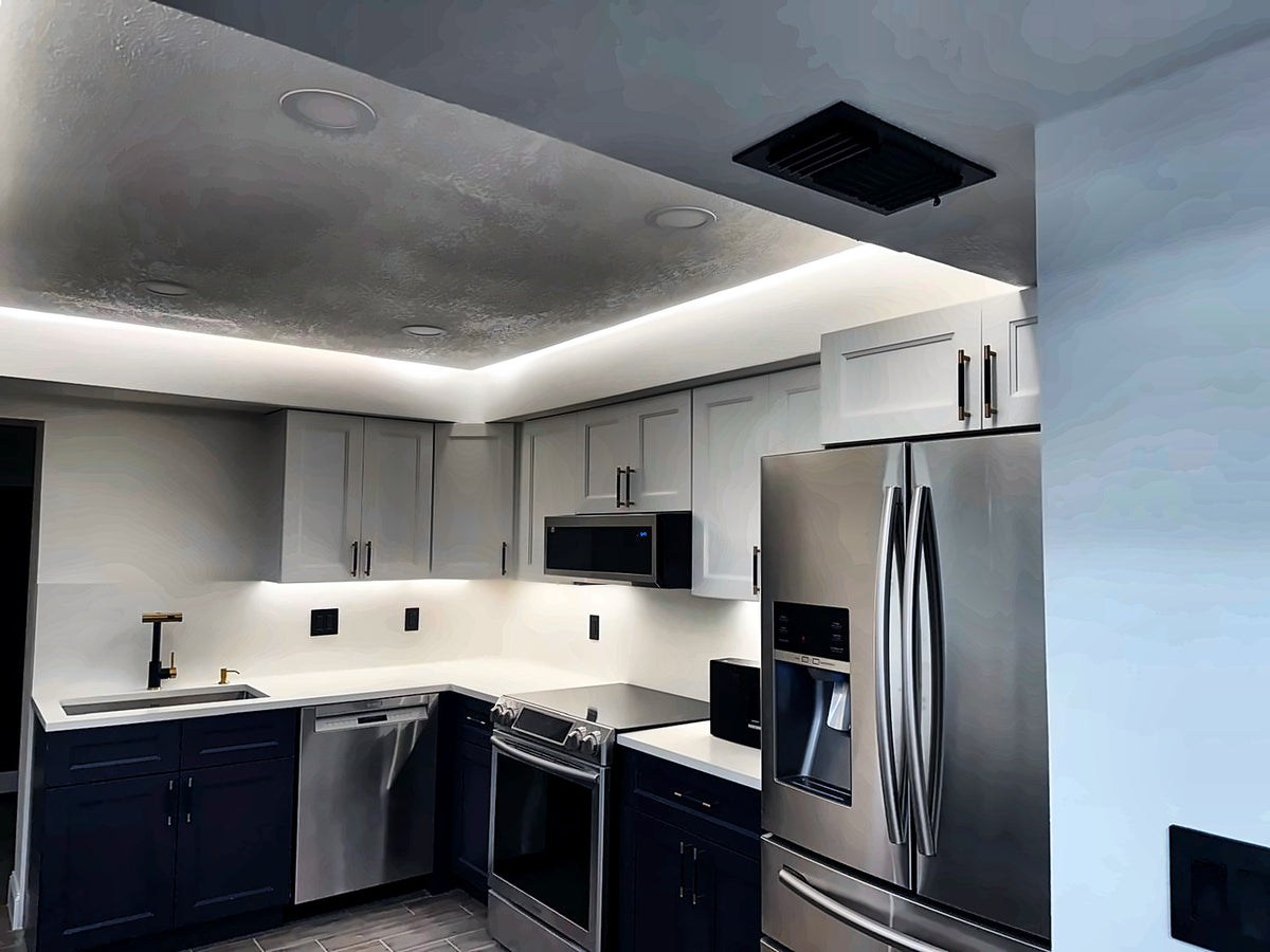 Finished kitchen with navy lower cabinets, white uppers, quartz counters, brass hardware and cove lighting