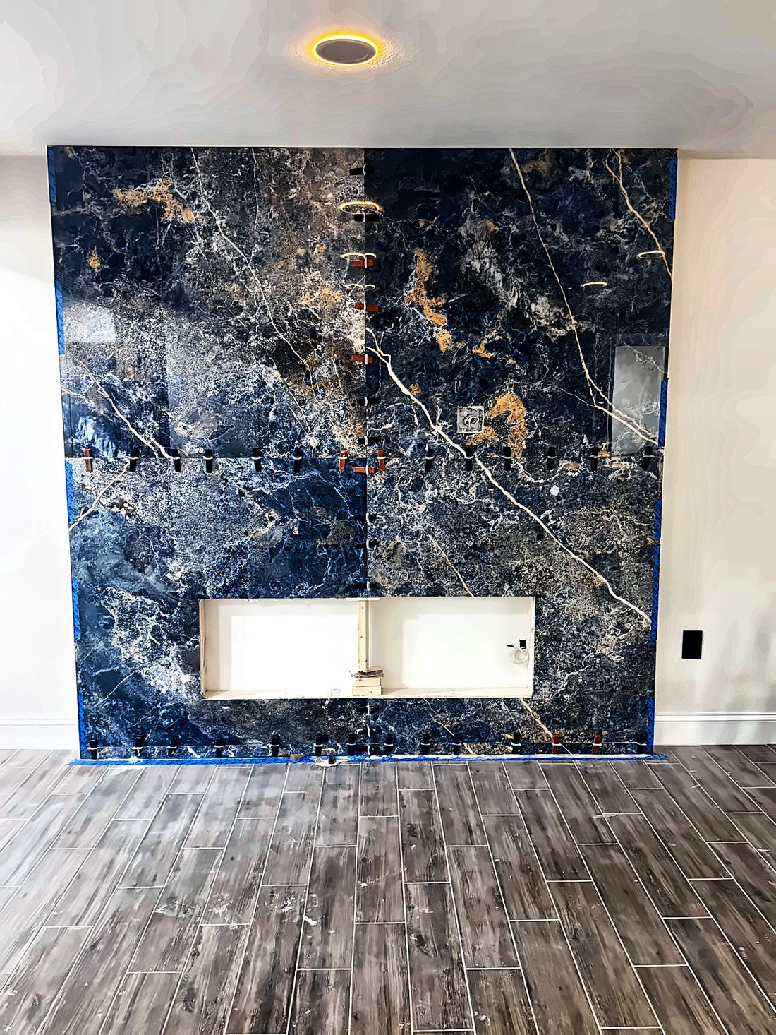 Large-format blue and gold marble-look slab being set with leveling clips still in place