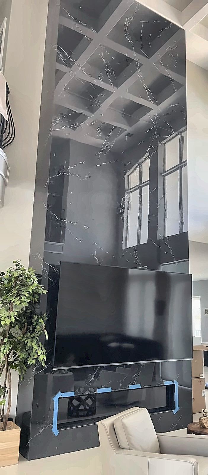 A two-storey feature wall in polished black marble slab with fine white veining, the coffered ceiling and arched windows reflected in it, with a television set into the face